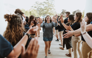 A first-year Gordon College student attending orientation and going down a line to receive high-fives from current students.